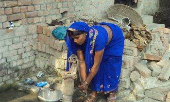 Frau schpft Wasser mit Handpumpe in Tirmasahun, Indien